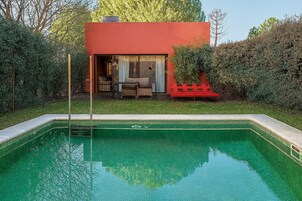 Piscina con un edificio rojo al fondo, rodeada de vegetación.