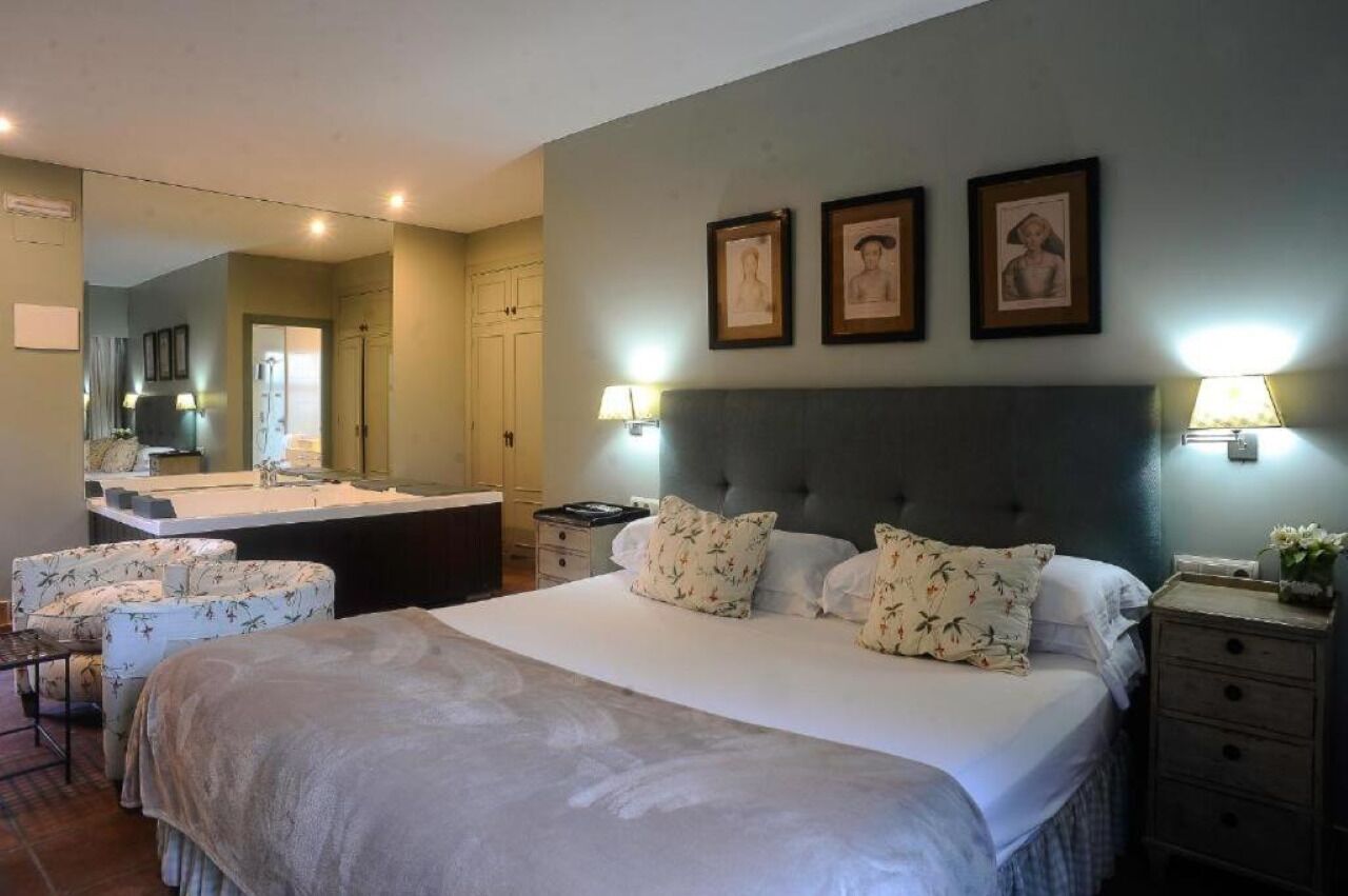 A bedroom with a large bed, a bedside table, a chair, a dresser, and a mirror.