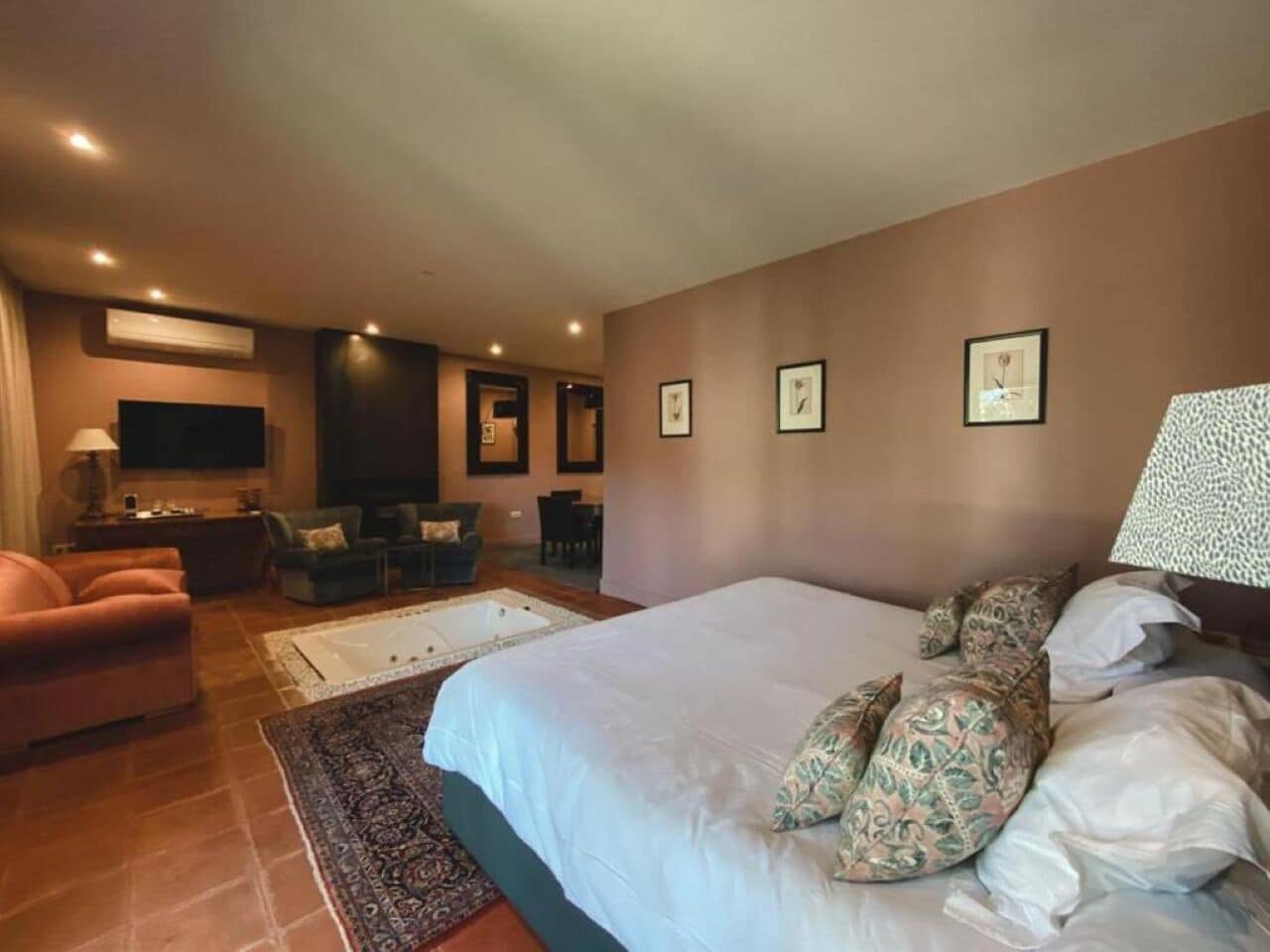 A spacious bedroom with a large bed, a sitting area with a sofa and chairs, a small table, and a wall-mounted TV.