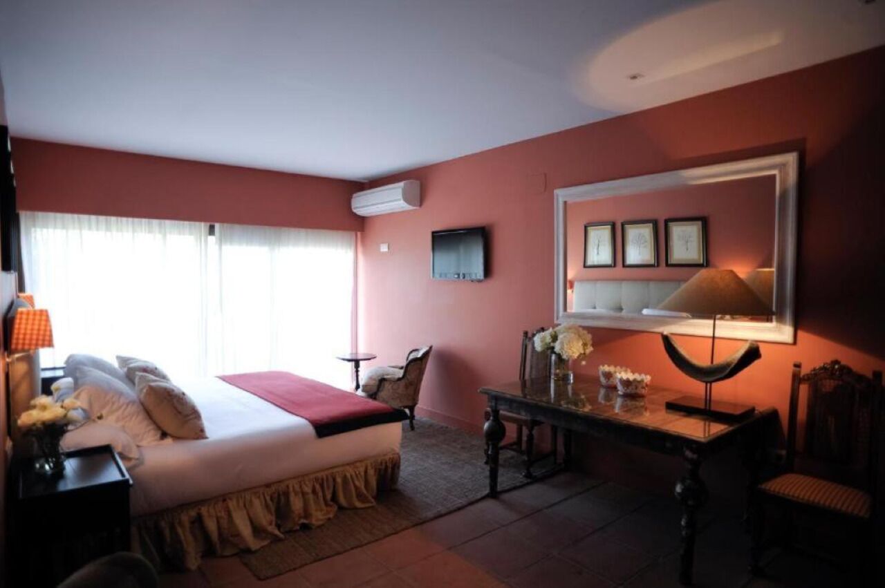 Un dormitorio con cama, mesita de noche, lámpara y televisor instalado en la pared.