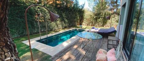A backyard with a swimming pool, wooden deck, and outdoor furniture.
