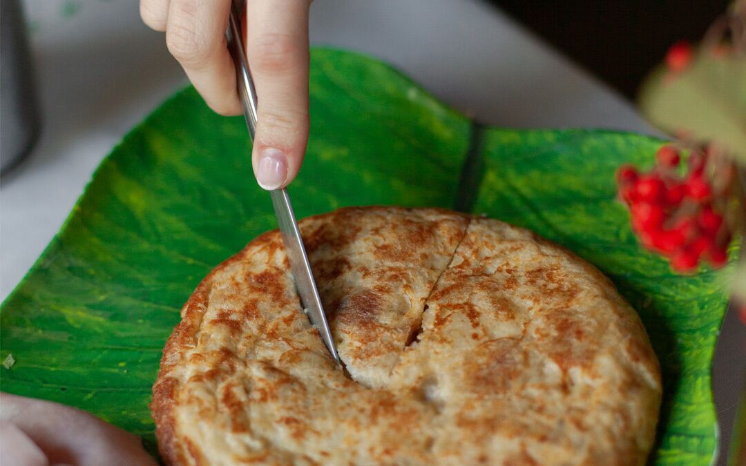 A hand cutting a round, golden-brown food item on a green leaf.