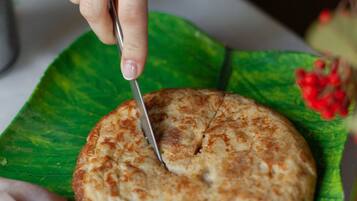 A hand cutting a round, golden-brown food item on a green leaf.