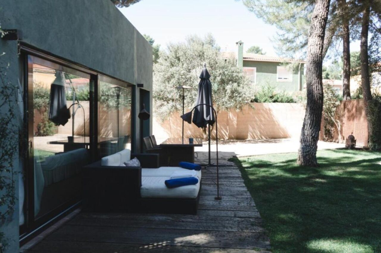 Un área de estar exterior moderna con una terraza de madera, un sofá y dos sombrillas.