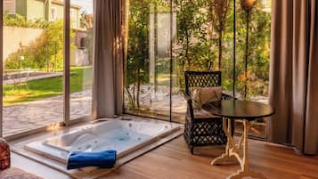 Een kamer met een grote glazen deur die uitkomt op een tuin, een houten vloer, een zwarte tafel met een stoel en een jacuzzi.