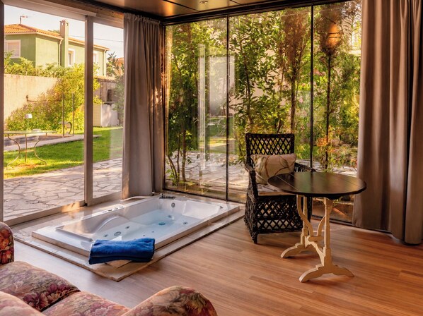 A room with a large glass door leading to a garden, a wooden floor, a black table with a chair, and a hot tub. - Hotel Boutique Pinar by Bossh Hotels (Jábaga)