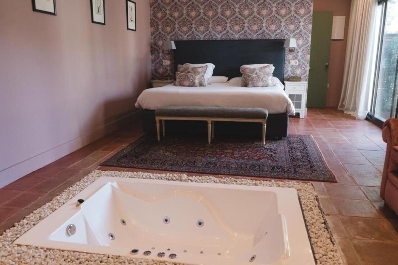 Een slaapkamer met een groot bed, nachtkastje, badkuip en een raam met gordijnen.
