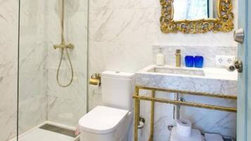 A modern bathroom with a glass-enclosed shower, a white toilet, a marble sink, and a gold-framed mirror.