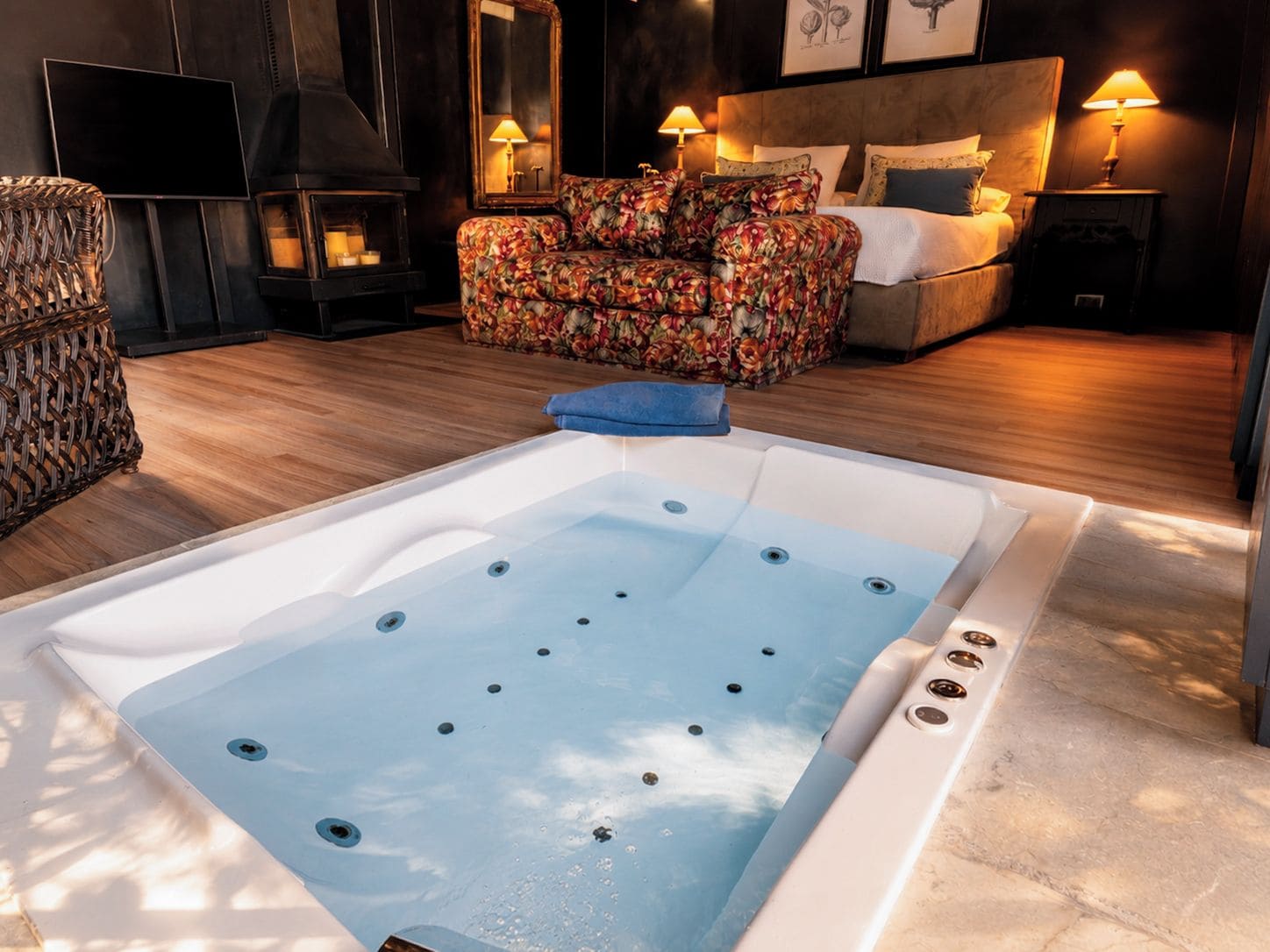 A modern bathroom with a large bathtub, a wicker chair, a sofa, and a bed with a headboard.