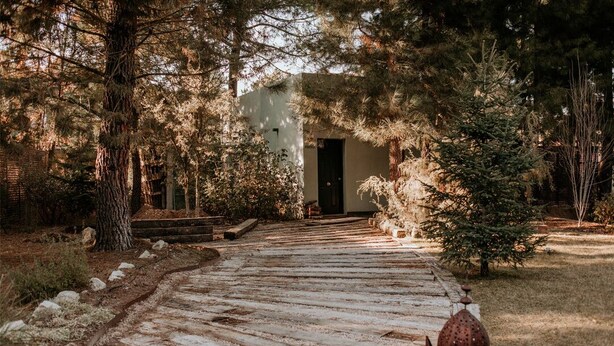 A rustic wooden pathway leading to a white building with a dark door, surrounded by trees and a small Christmas tree. - Hotel Boutique Pinar by Bossh Hotels (Jábaga)