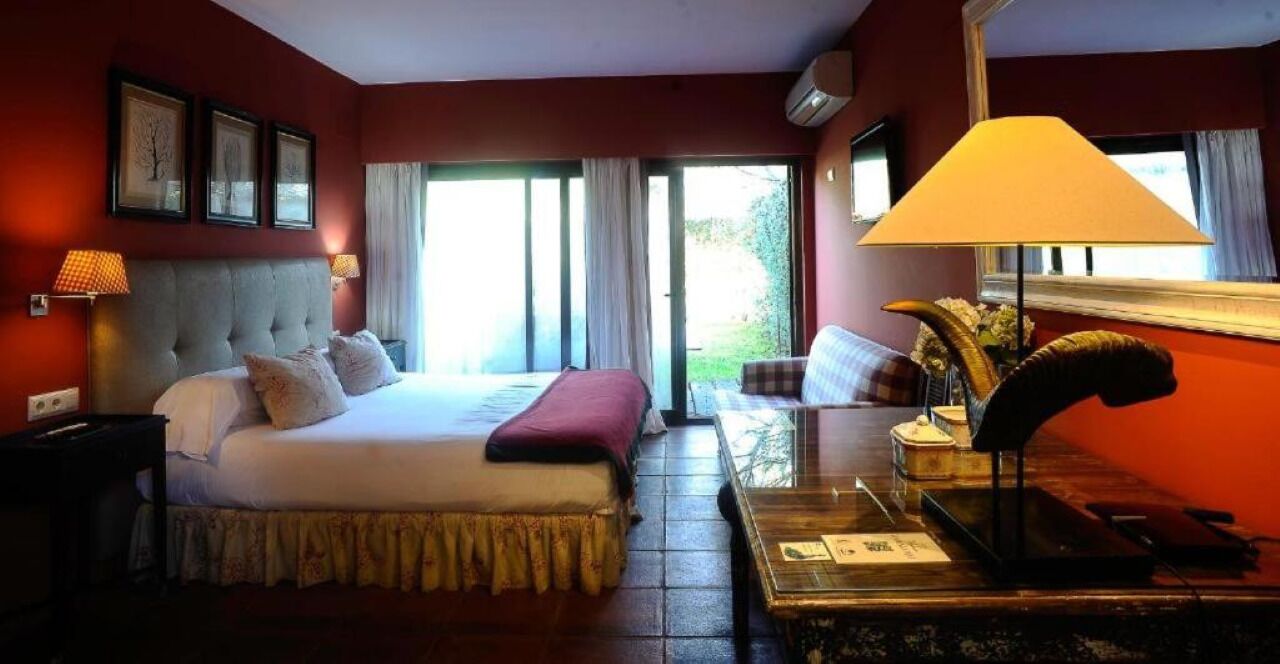 Habitación de hotel con una cama grande, un escritorio con lámpara, una silla y vistas al exterior a través de una puerta corrediza.