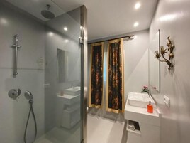 Un baño moderno con ducha de vidrio, lavamanos blanco y espejo con detalles decorativos.
