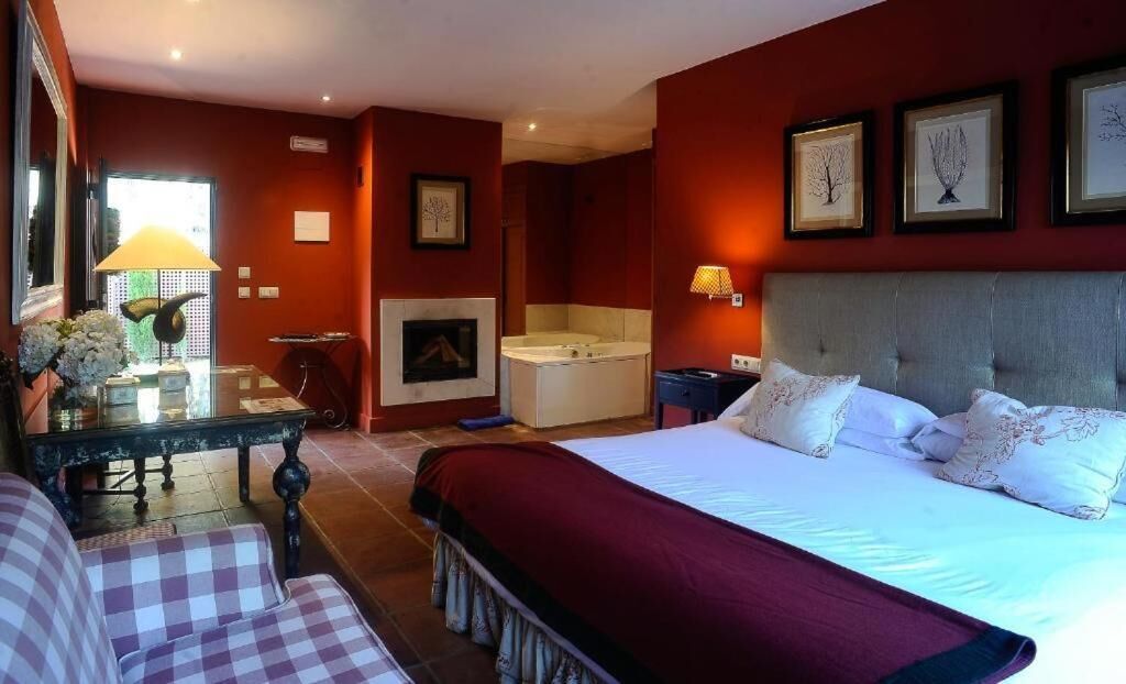 Una habitación de hotel con una cama grande, un área de estar con una mesa y sillas, chimenea y una bañera.