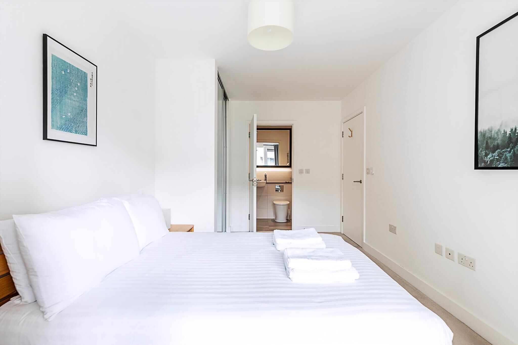 A hotel room with a bed, a bathroom visible through an open door, and a framed picture on the wall.