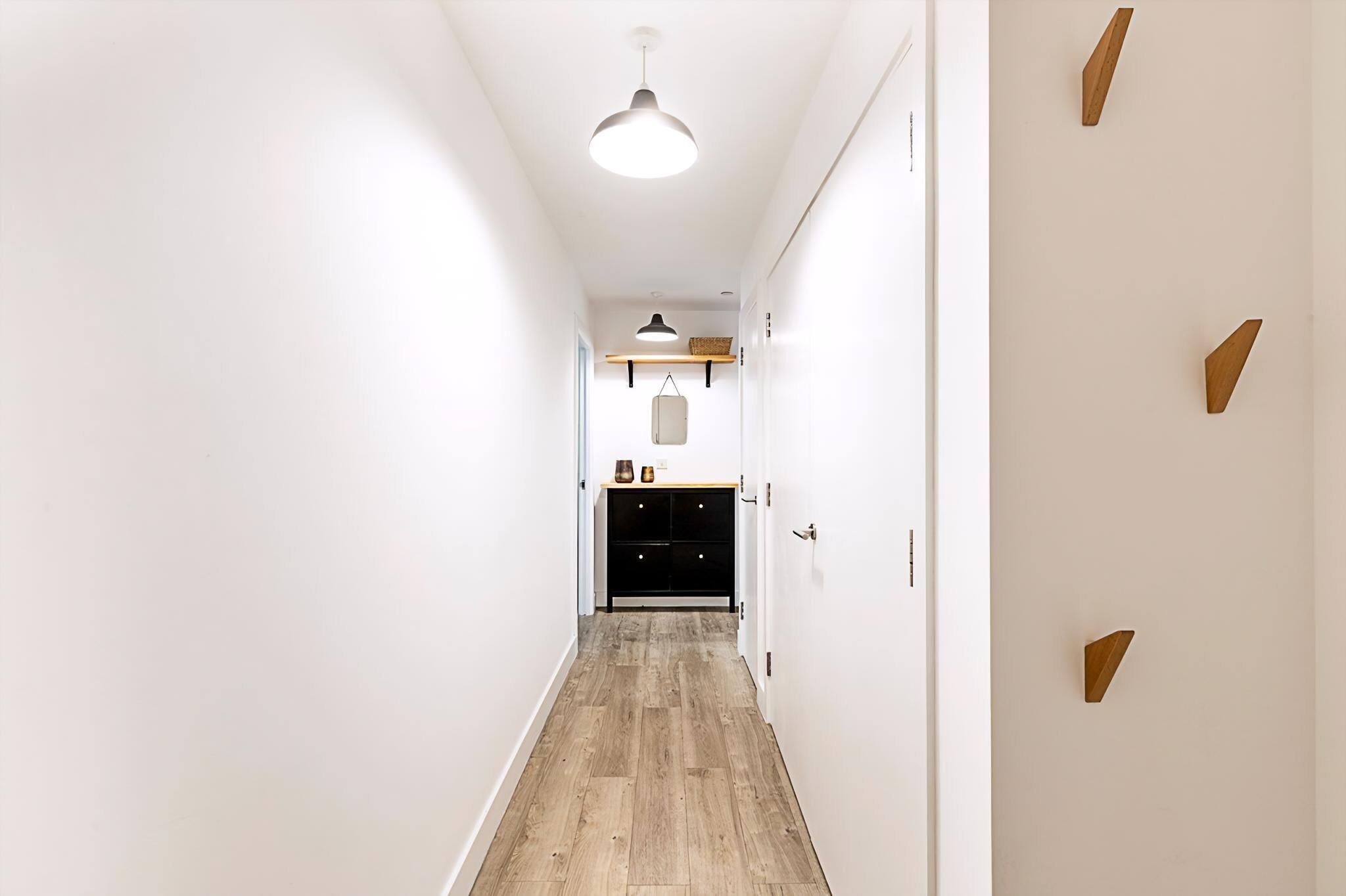 A hallway with a wooden floor, white walls, and a black cabinet with drawers.