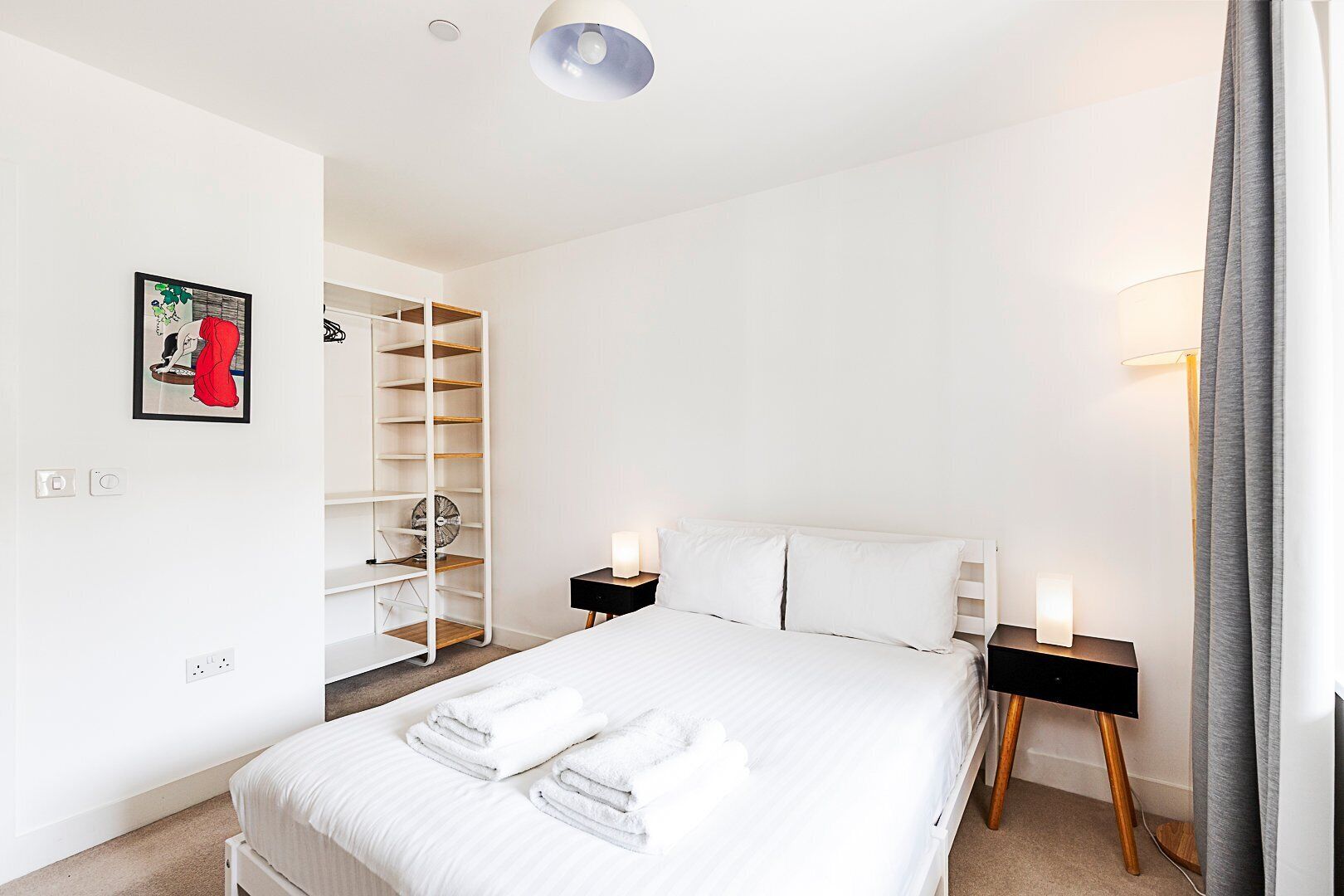 A modern hotel room with a large bed, a built-in wardrobe, bedside lamps, and a framed picture on the wall.