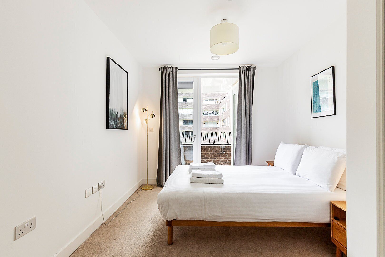 A bedroom with a bed, a bedside table, a floor lamp, and a window with curtains.