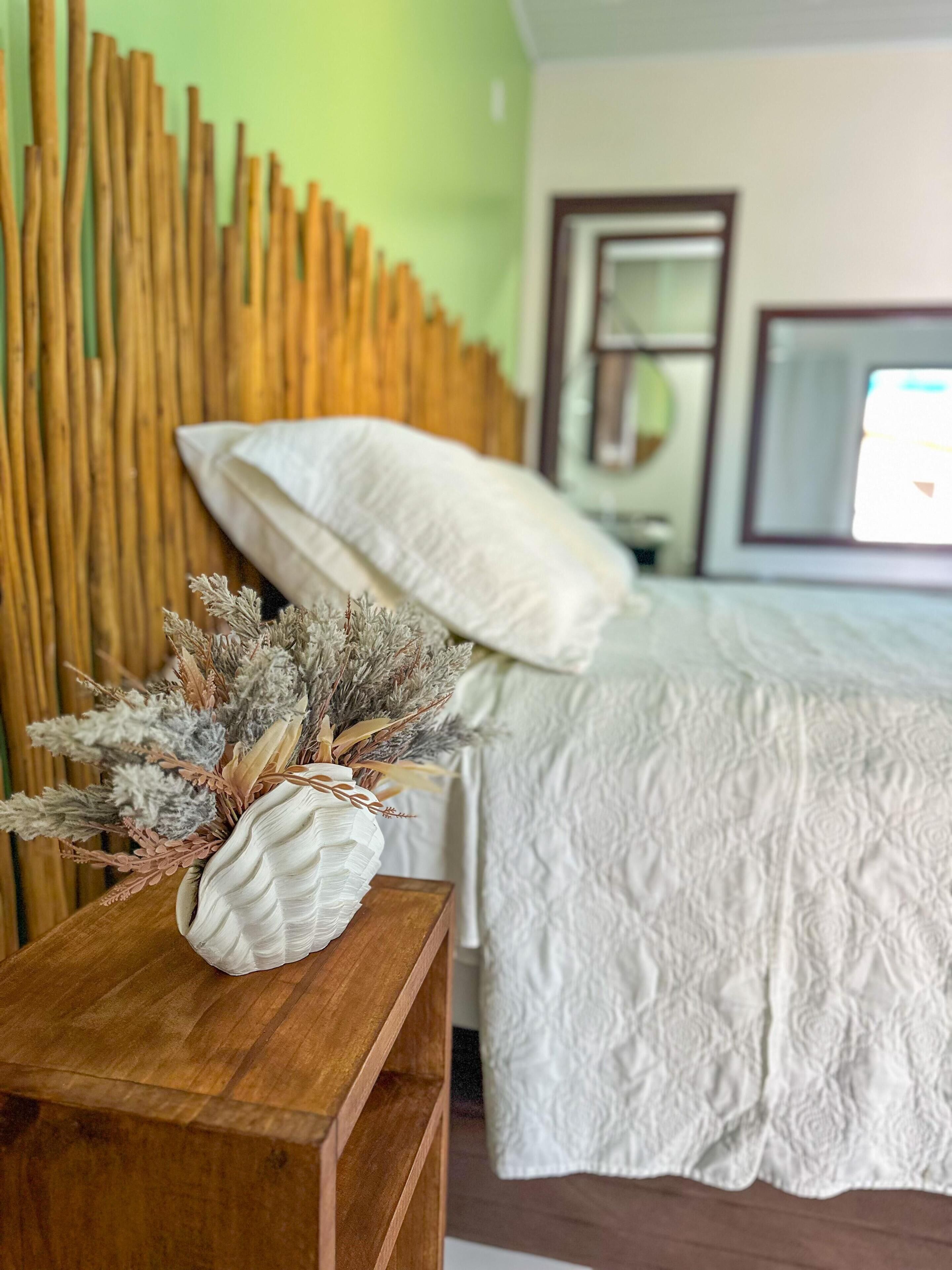 A bedroom with a wooden headboard, a bed with white bedding, and a wooden nightstand with decorative dried plants.