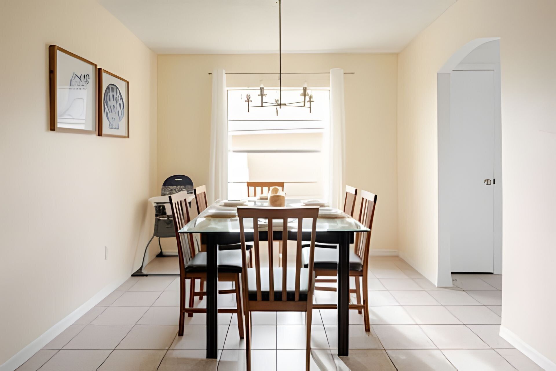 Un'area pranzo con un tavolo rettangolare, sei sedie di legno, un lampadario e una finestra con tende.