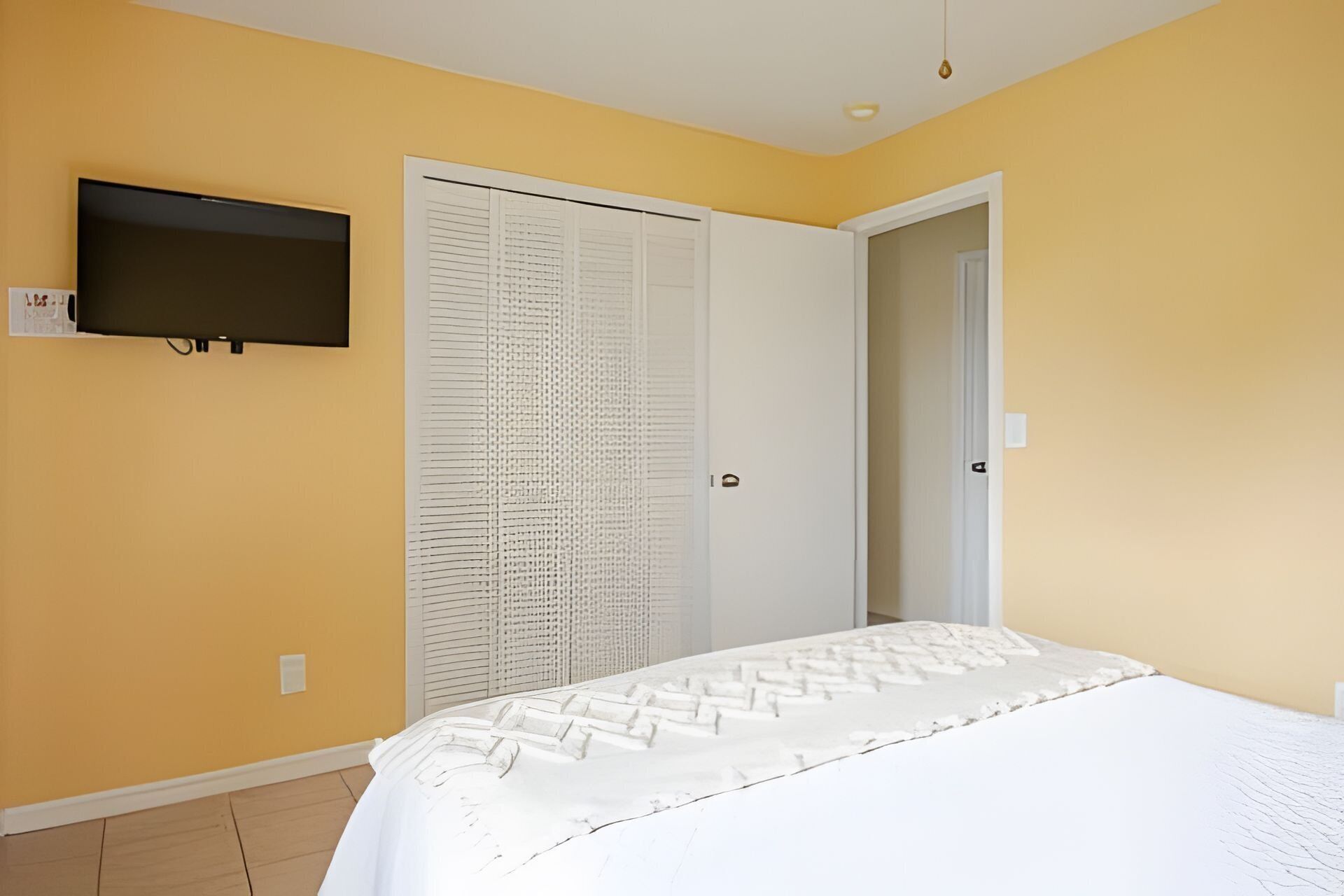 A bedroom with a bed, a television mounted on the wall, and a white door with a louvered window.