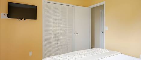 A bedroom with a bed, a television mounted on the wall, and a white door with a louvered window.