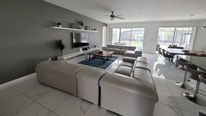 A modern living room with a sectional sofa, a flat-screen TV, and a dining area with a table and chairs. - Fantastic Large Pool,Sonoma Resort (Kissimmee)