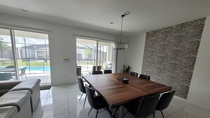 A modern dining area with a wooden table and black chairs, large windows, and a view of a swimming pool. - Fantastic Large Pool,Sonoma Resort (Kissimmee)