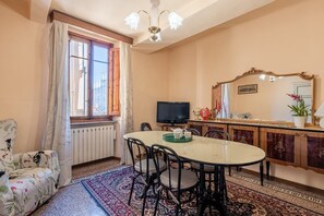 A dining area with a round table, chairs, a television, a cabinet with a mirror, and a radiator.