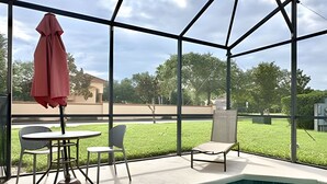 Zona de piscina con cerramiento de vidrio, una mesa con sillas y una sombrilla roja.