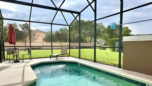Una piscina con cerramiento de vidrio, una silla de descanso y una sombrilla roja.