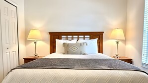 Una cama bien hecha con una colcha estampada y almohadas, flanqueada por dos lámparas de noche sobre mesitas de madera.