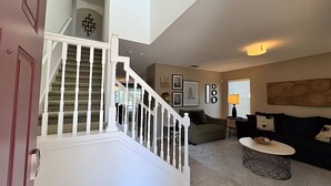A staircase leading to a second floor, a living room with a sofa, a coffee table, and wall art. - New to Market Spacious Private Pool Retreat (Kissimmee)