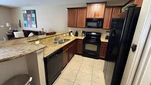 A compact kitchen with wooden cabinets, a black refrigerator, a microwave, a dishwasher, and a tiled floor. - New to Market Spacious Private Pool Retreat (Kissimmee)