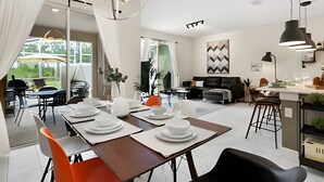 A modern dining area with a wooden table set for four, surrounded by chairs. A large window provides a view of greenery outside. - Champions Gate, Pool Home near Disney (Kissimmee)