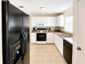 A kitchen with white cabinets, a black refrigerator, a stove, a microwave, and a sink.