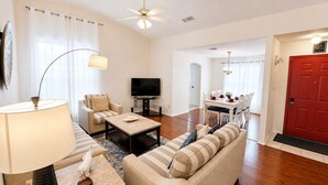 A living room with a sofa, coffee table, TV, and a dining area with a table and chairs.