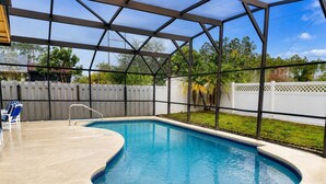 A swimming pool with a curved edge, surrounded by a covered area with a metal frame and glass panels.