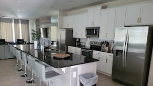 A modern kitchen with white cabinets, stainless steel appliances, a central island with bar stools, and a trash bin. - Renovated Themed Bedrooms, Game Room, Pool (Kissimmee)