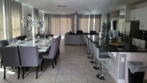 A modern kitchen with a central island, dining area with a long table, and a seating area with a sofa. - Renovated Themed Bedrooms, Game Room, Pool (Kissimmee)