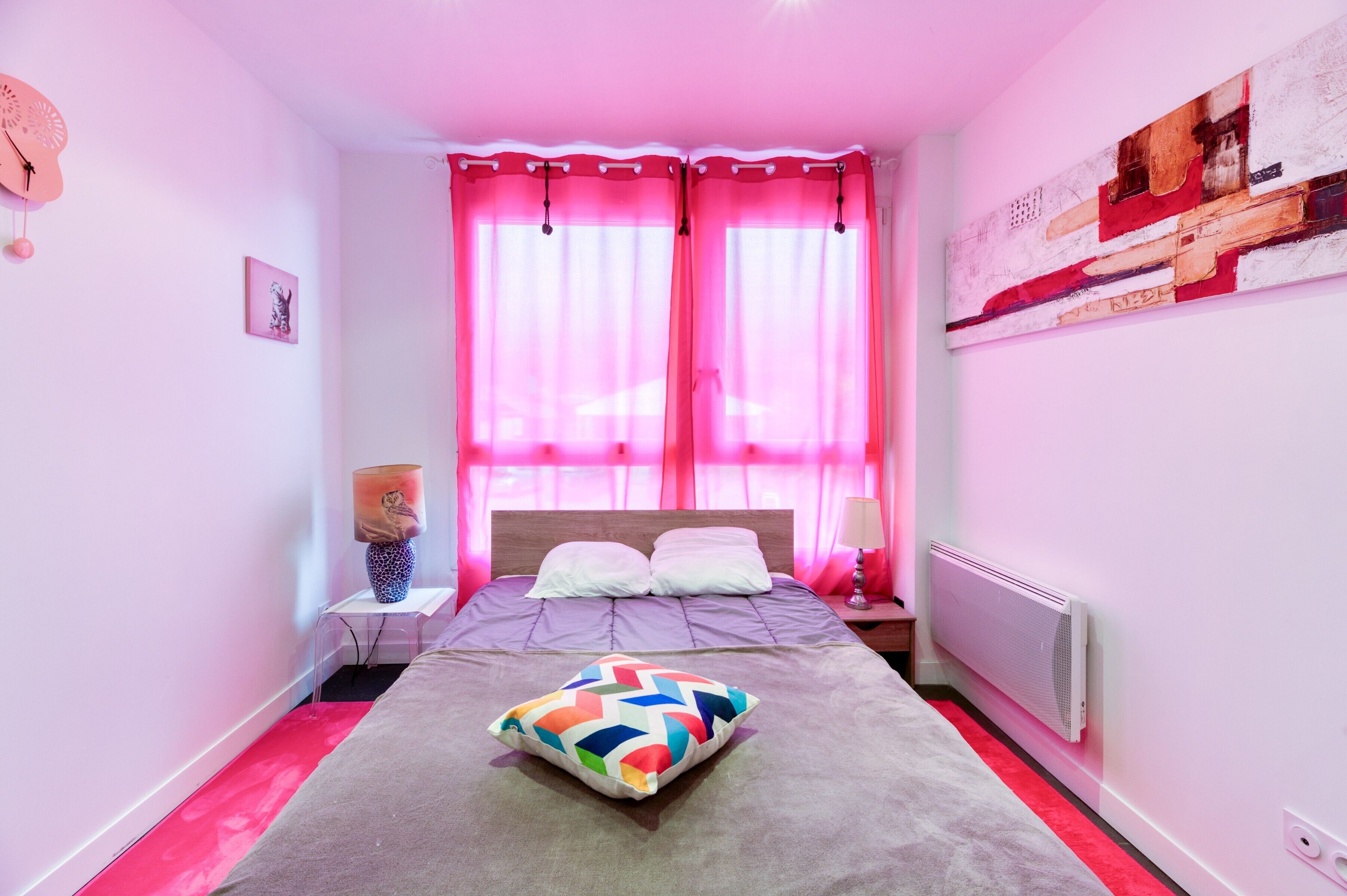 Ein Schlafzimmer mit einem Bett, rosa Vorhängen, einem Heizkörper und einem Bild an der Wand.