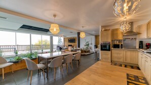 Een moderne keuken met houten kasten, een eethoek met een lange tafel en stoelen, en een groot raam dat voor natuurlijk licht zorgt.