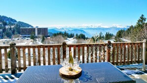 Een balkon met een gedekte tafel voor een maaltijd, met uitzicht op een bergachtig landschap en een gebouw op de achtergrond.