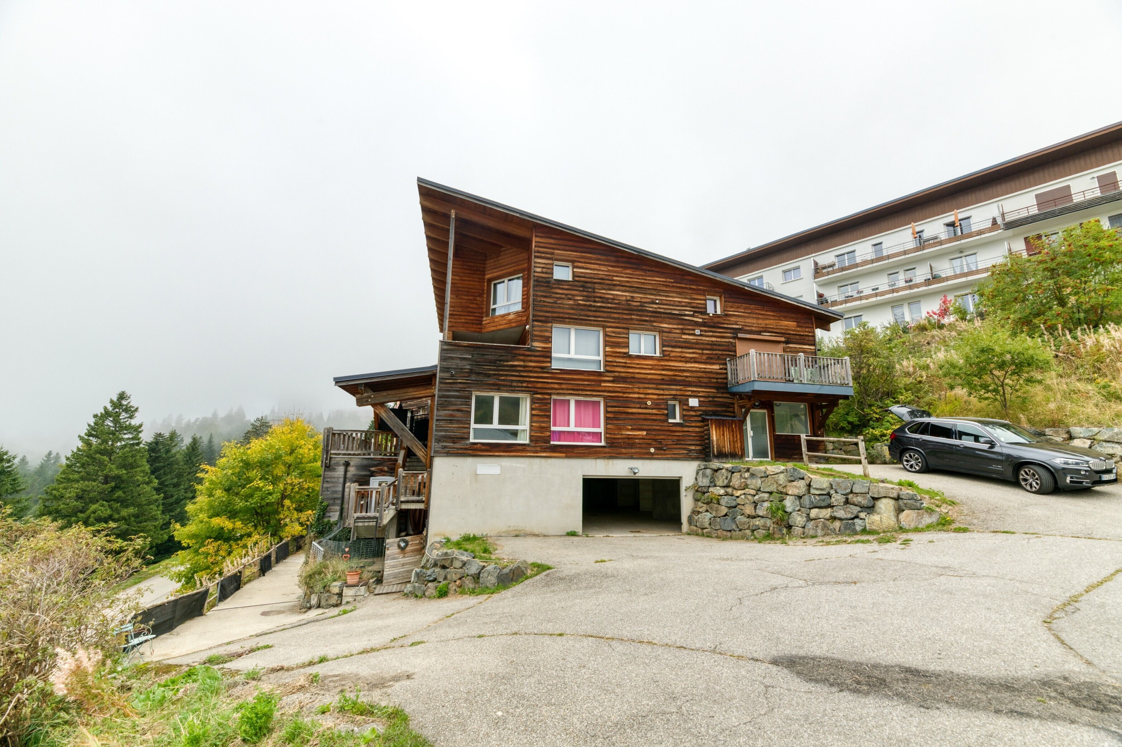 Un bâtiment moderne en bois, doté d’un toit en pente, d’un mur en pierre et d’une voiture garée devant.