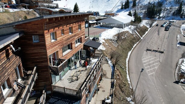 A multi-story wooden building with balconies, a ski slope in the background, and a parking area. - Dream Vacation – Couples, Right by the Slopes (chamrousse)