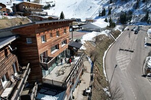Un edificio de madera de varios pisos con balcones, una pista de esquí al fondo y un área de estacionamiento.