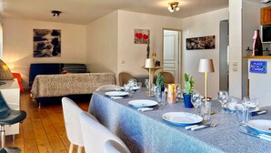 Un coin repas avec une table dressée pour quatre personnes, un canapé, une lampe et un panneau indiquant l’endroit où l’on prend l’apéritif.