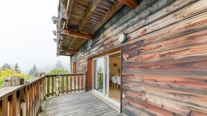 Une cabane en bois dotée d’une terrasse, d’une porte-fenêtre coulissante et d’un intérieur visible, avec une table et des chaises.