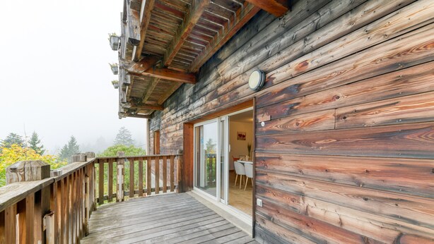 Une cabane en bois dotée d’une terrasse, d’une porte-fenêtre coulissante et d’un intérieur visible, avec une table et des chaises.