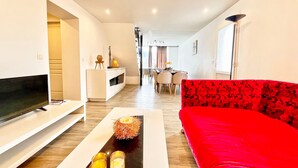 A living room with a TV, a red sofa, a white console, and a dining area in the background. - Dream Holiday Apartment - Casserousse - 18 Guests at the Foot of the Slopes (chamrousse)