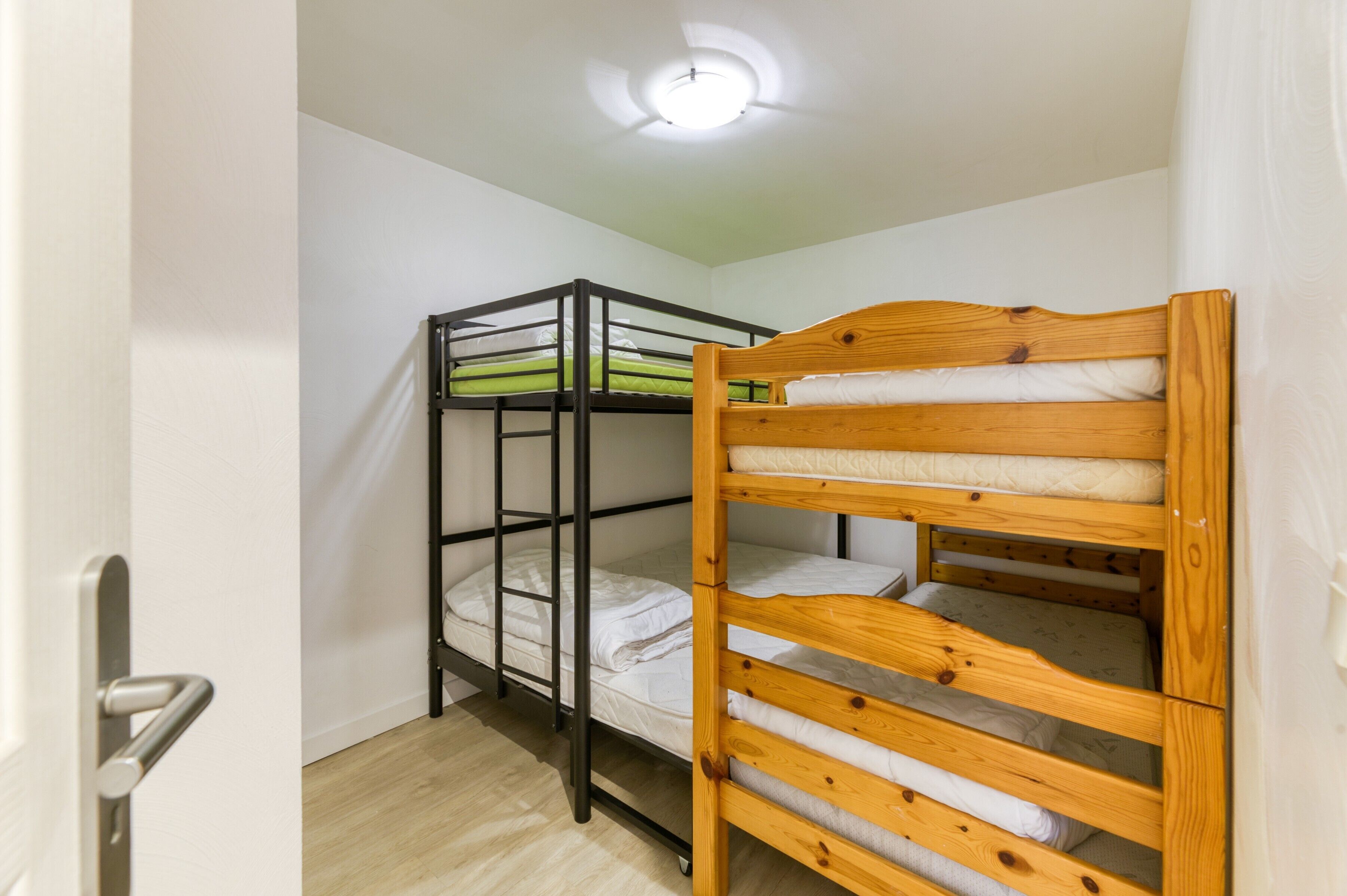Een kamer met stapelbedden, een deur en een plafondlamp.